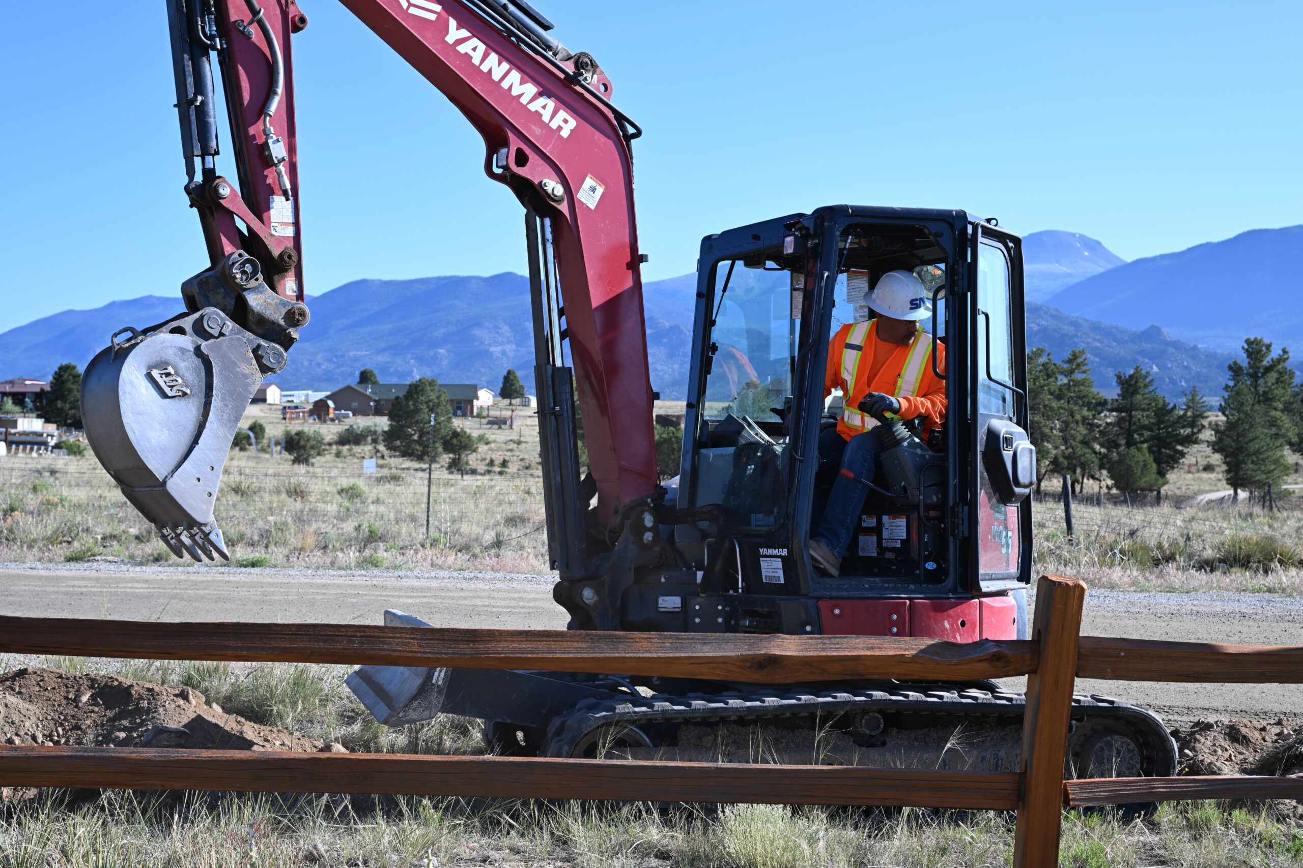 Construction worker operating a red Yanmar excavator during FTTH fiber installation in Buena Vista.
